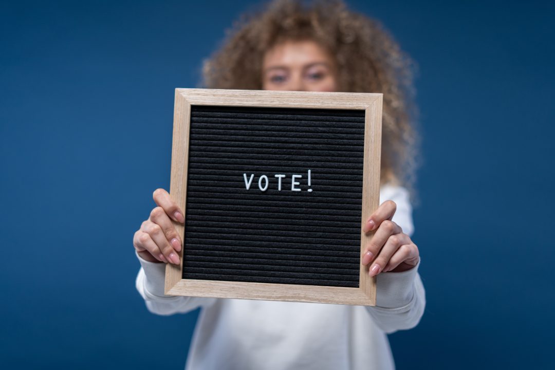 girl holding a bulletin that says 'VOTE!'